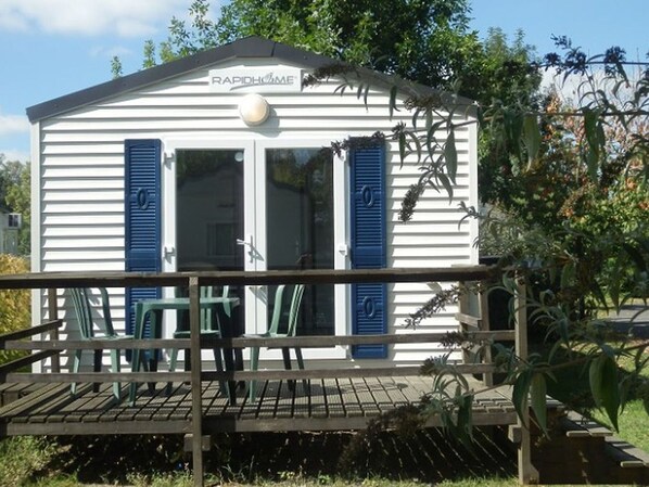 Un bâtiment blanc avec des volets bleus, une enseigne indiquant « RapidHome », et une terrasse en bois avec des chaises.