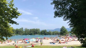 Ein Strand mit badenden Personen, umgeben von Bäumen und einem klaren Himmel.