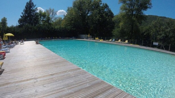 A wooden deck leading to a clear blue pool surrounded by trees.