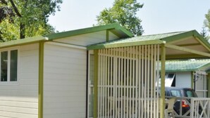 A small, single-story wooden cabin with a green roof and a fenced porch.