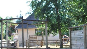 A wooden play structure with climbing elements and a fenced area.