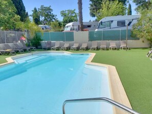 A swimming pool with a metal ladder, surrounded by green artificial grass and white lounge chairs. - Cozy Mobile Home - 2 Bedrooms, Terrace, Sleeps 4 (Le Pradet)