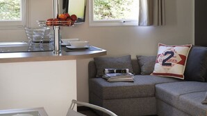Ett modernt vardagsrum med en grå soffa, ett litet bord med en kopp och ett fat, och ett fönster med gardiner.