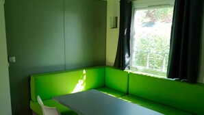 Ein Zimmer mit einem grünen Sofa und einem kleinen Tisch. Ein Fenster mit Vorhängen ist vorhanden.