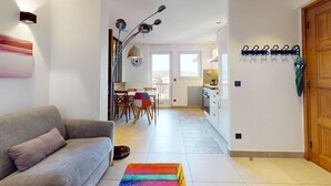Un salon moderne avec un canapé gris, un tapis coloré et un coin repas comprenant une table et des chaises.