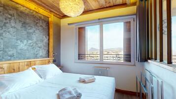 Ein Schlafzimmer mit Holzboden, einem großen Fenster mit Blick und einem Bett mit weißer Bettwäsche, sowie einem Heizkörper.