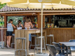 Ein Außenbereich mit Bar, Holzmöbeln und einem gelben Sonnenschirm.