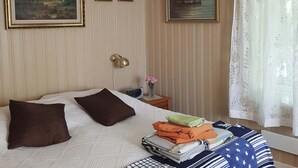 Ein ordentlich eingerichtetes Schlafzimmer mit einem Bett, Kissen, einem Nachttisch mit Lampe und zwei gerahmten Bildern an der Wand.