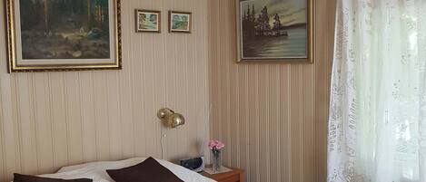 Een keurig opgemaakt slaapkamer met een bed, kussens, een nachtkastje met een lamp en twee ingelijste foto's aan de muur.