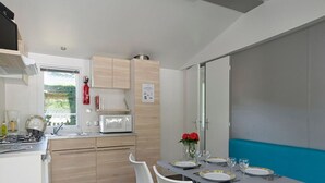 A compact kitchen with a dining area, including a table set for two with plates, glasses, and a vase of flowers. - Cozy mobile home for 4 people with fully-equipped kitchen (Les Aires)
