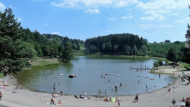 A lakeside setting with people swimming and relaxing on the shore.