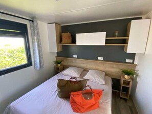 Une chambre à coucher avec un lit, deux tables de chevet, une fenêtre et une étagère fixée au mur, sur laquelle se trouvent un sac et un panneau.