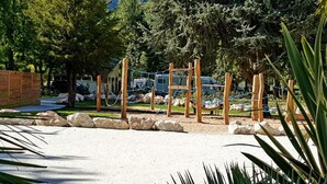 Een speeltuin met houten constructies en touwen, omringd door bomen en rotsen.