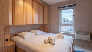 Een slaapkamer met een groot bed, houten hoofdbord en een raam met uitzicht over de stad.