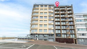 Een meerlaags hotel met een modern design, met een restaurant op de begane grond en een parkeerplaats met fietssymbolen.