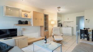 Een moderne woonkamer met een televisie, bank, glazen salontafel en een eethoek met stoelen en een tafel.