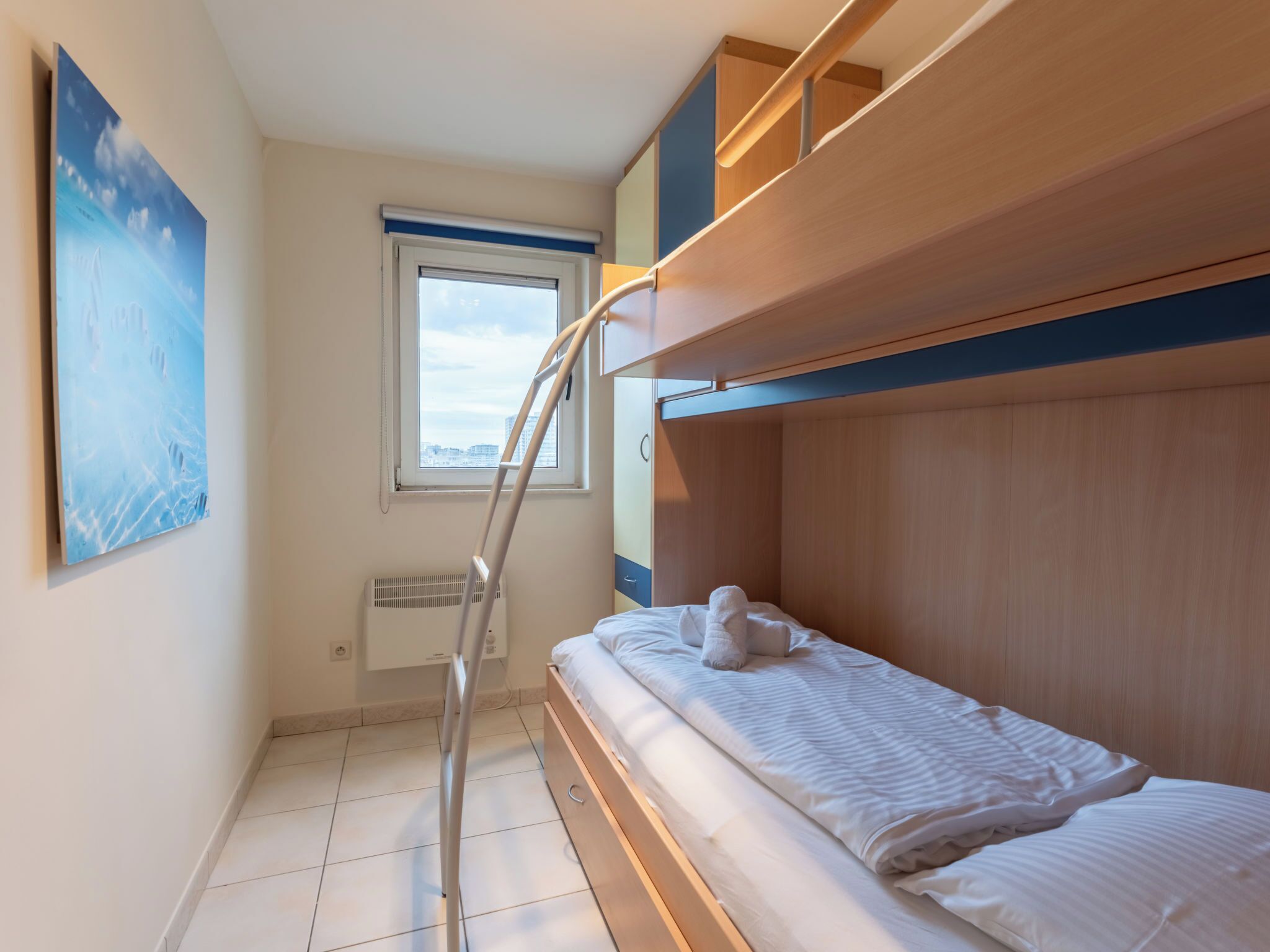A bunk bed with a ladder, a window with a view, and a radiator.