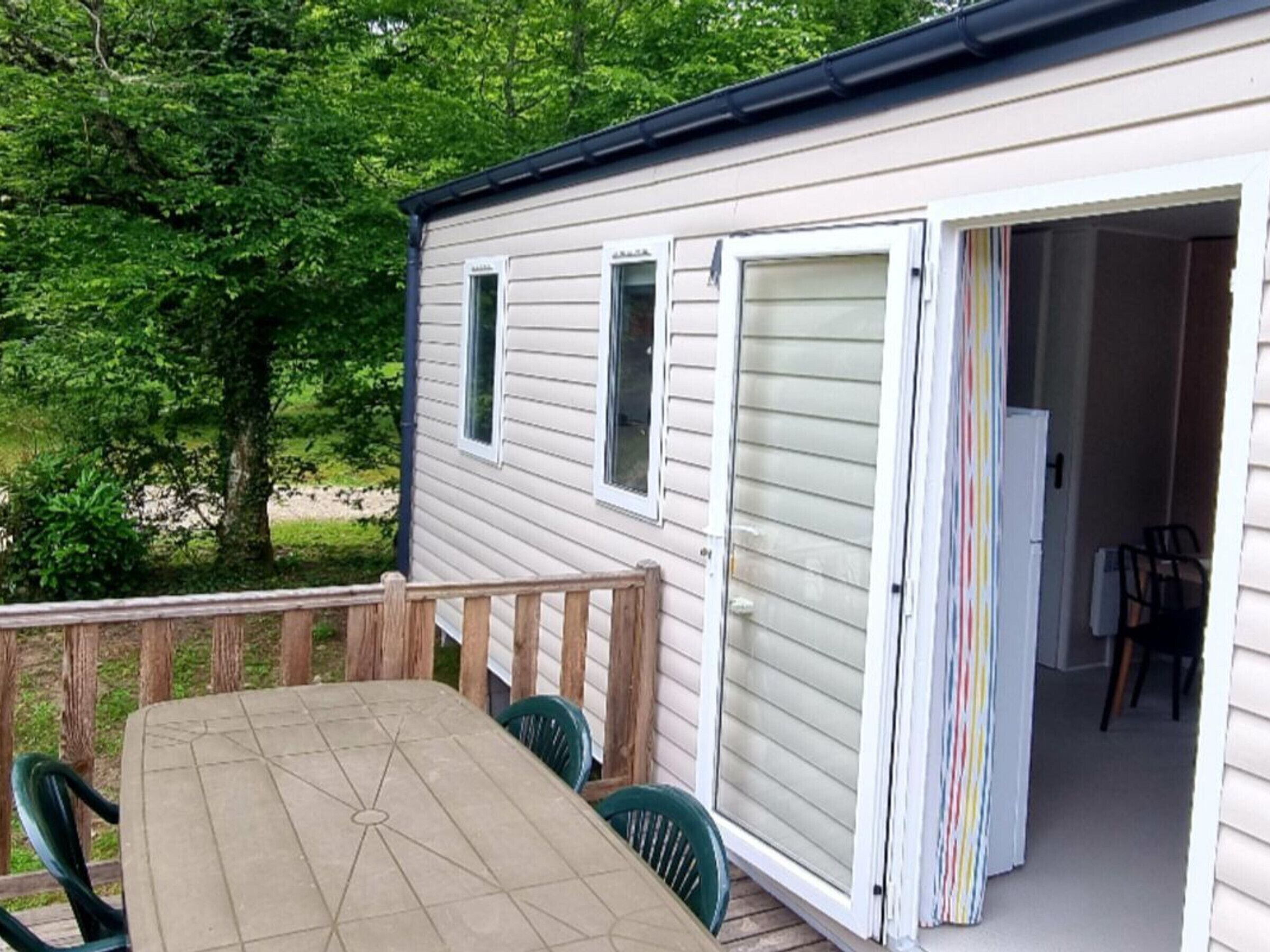 A small, single-story cabin with a wooden deck and a sliding door leading to an interior with a dining area.