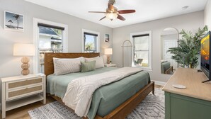 Quarto com cama de madeira, duas mesas de cabeceira, ventilador de teto e uma janela grande.