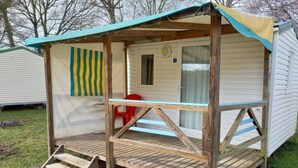 Een stacaravan met een veranda, een rode stoel en een gestreept zonnescherm.