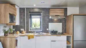 A modern kitchen with white cabinets, a black backsplash, a window, and a stainless steel refrigerator. - Mobile home 4 guests - 2 bedrooms - Terrace (Saint-Julien-en-Born)