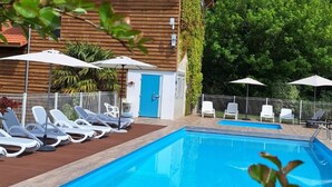 A rectangular swimming pool with a wooden deck, surrounded by white lounge chairs and umbrellas. - Mobile home 4 guests - 2 bedrooms - Terrace (Saint-Julien-en-Born)