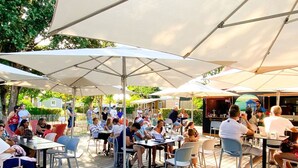 An outdoor patio area with tables and chairs under large umbrellas, surrounded by greenery. - Mobile Home with Terrace for 4 ppl, 2 BR (Dolus-d'Oléron)