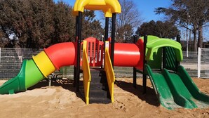 Une aire de jeux avec un toboggan, une structure d’escalade et un espace sablonneux.