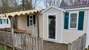 Ein kleines, eingeschossiges Mobilheim mit Holzterrasse und überdachter Veranda.