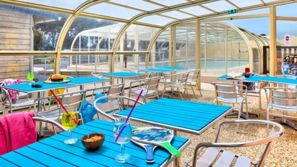A greenhouse-style restaurant with tables and chairs, large windows, and a view of the outside. - Mobile home for 6 with terrace in Sainte-Marie-du-Mont (Sainte-Marie-du-Mont)