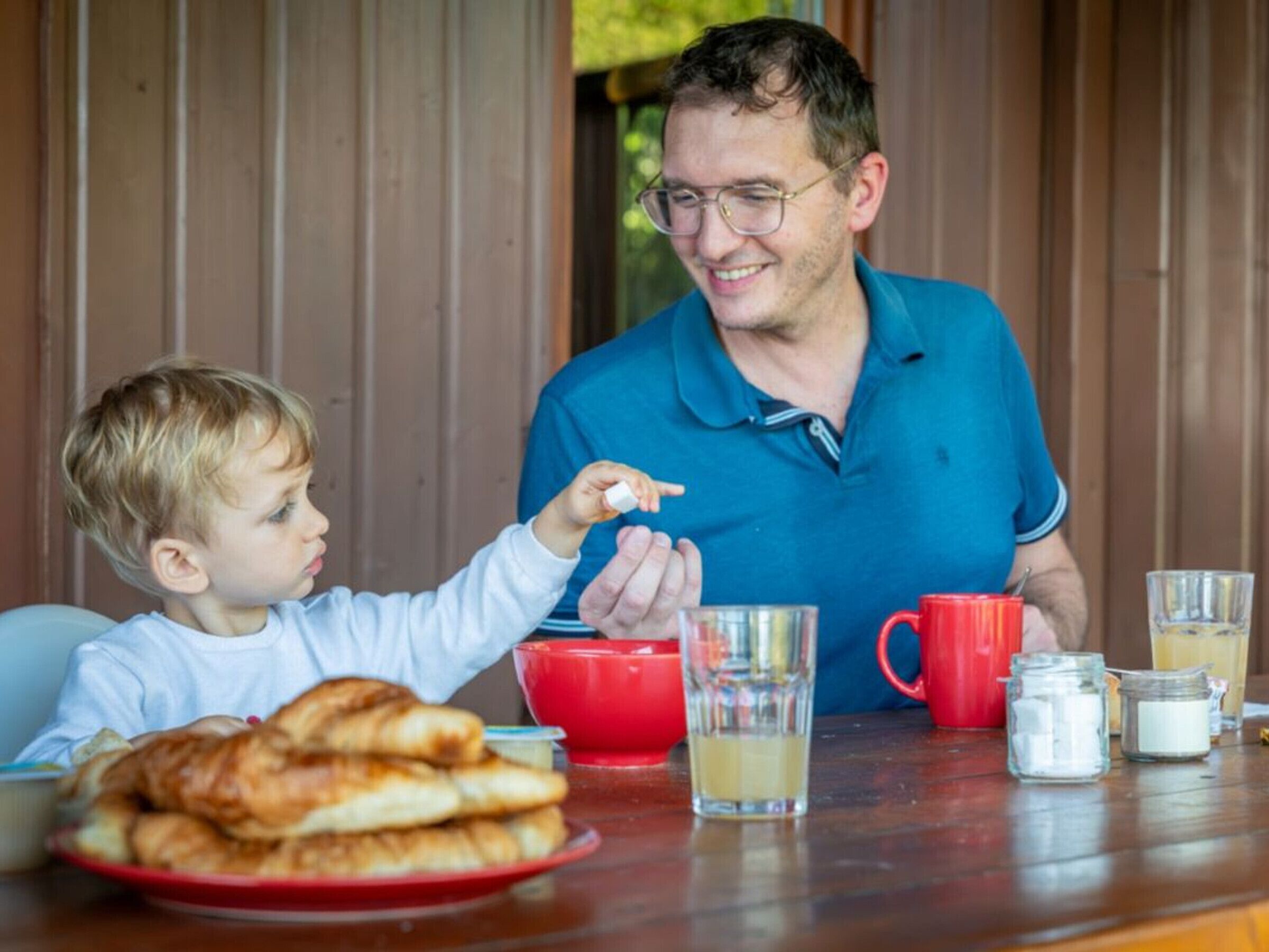 Uma mesa de jantar com um prato de croissants, uma caneca vermelha e um copo de suco.