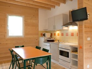 A compact kitchen with wooden walls, a dining table, chairs, a microwave, a stove, and a TV mounted on the wall. - Spacious Chalet with Terrace for 8 People (Dienné)