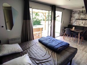 Ein Hotelzimmer mit Bett, Schreibtisch und Stuhl. Es gibt ein Fenster mit Vorhängen, einen Spiegel und eine Wand mit Muster.