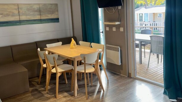 Ein Essbereich mit Holztisch und -stühlen, einem an der Wand befestigten Flachbildfernseher und Blick auf die Terrass'.