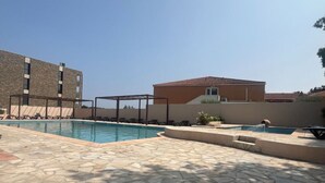 Ein Schwimmbecken mit Liegestühlen und einer Pergola, umgeben von Steinplatten und Gebäuden.
