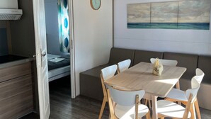 Ein Zimmer mit Holztisch und weißen Stühlen, einem Bett mit blau-weißer Vorhang und einem Landschaftsbild an der Wand.