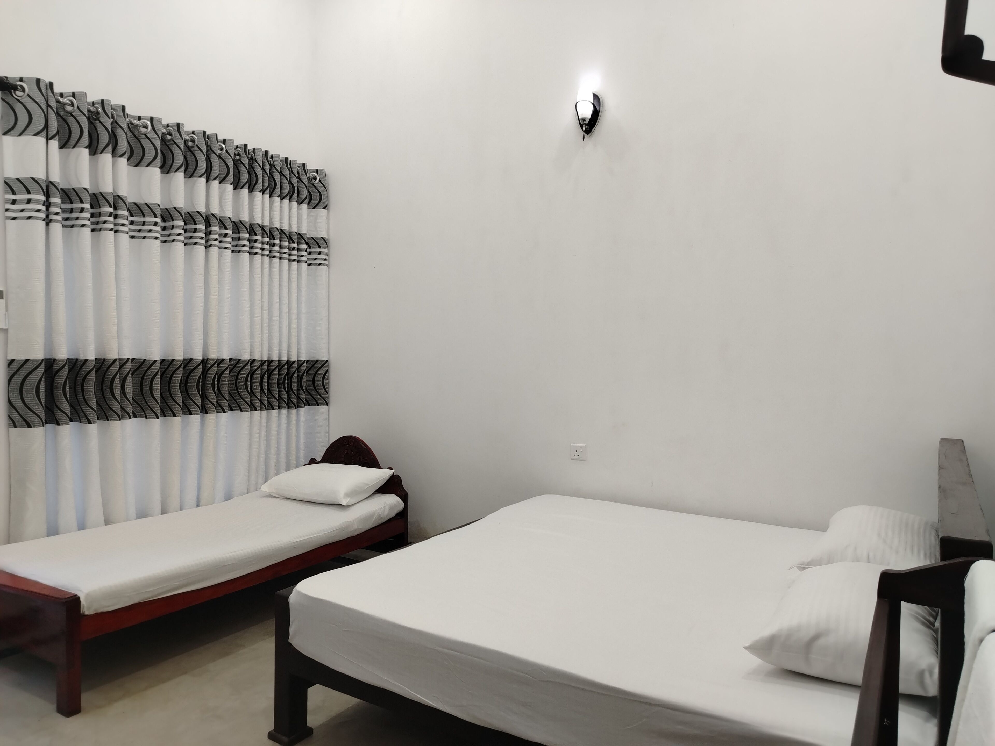 A room with two single beds, a wall-mounted light, and a curtain with a black and white pattern.