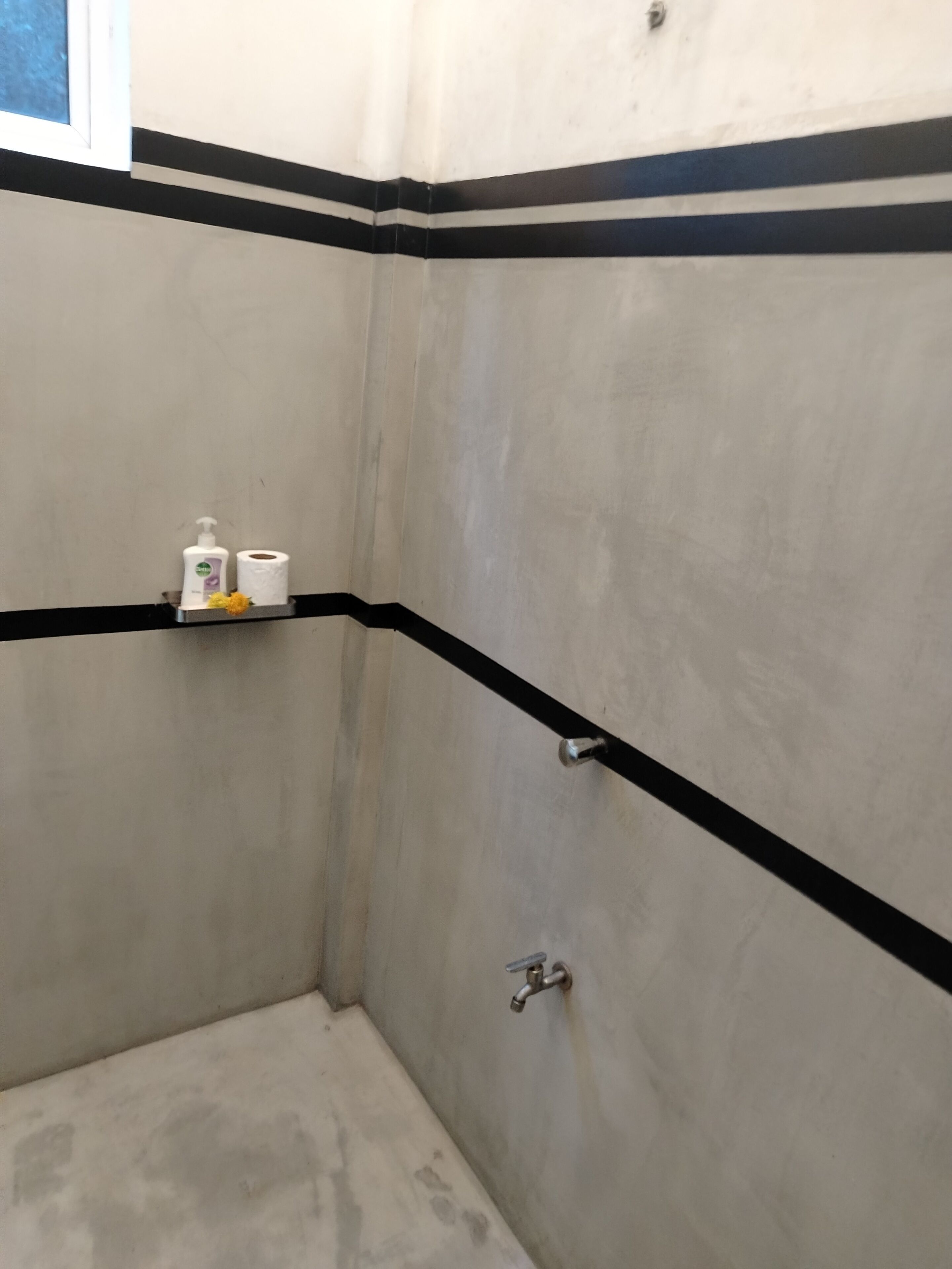 A bathroom with a white tiled wall, a black stripe, a shelf with toiletries, and a shower door.
