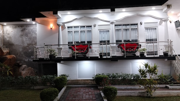 A modern building with a balcony, potted plants, and a brick pathway leading to the entrance. - Hotel Diamond Palace  (Bibile)
