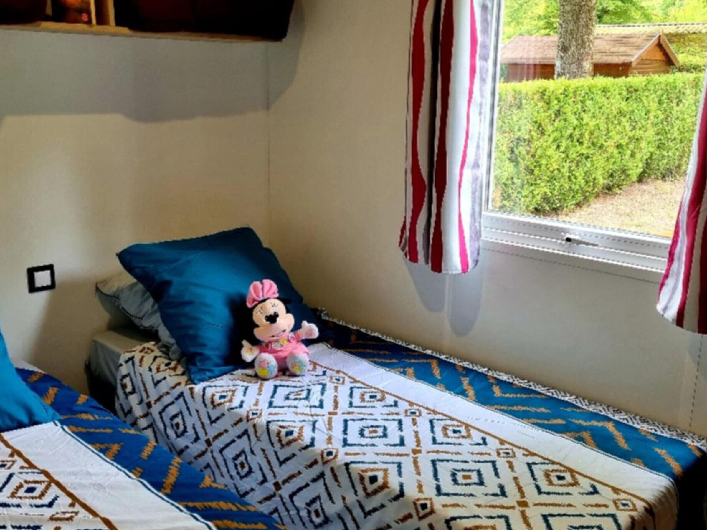 Een knus kamertje met een bed, een raam met gordijnen en uitzicht op groen.
