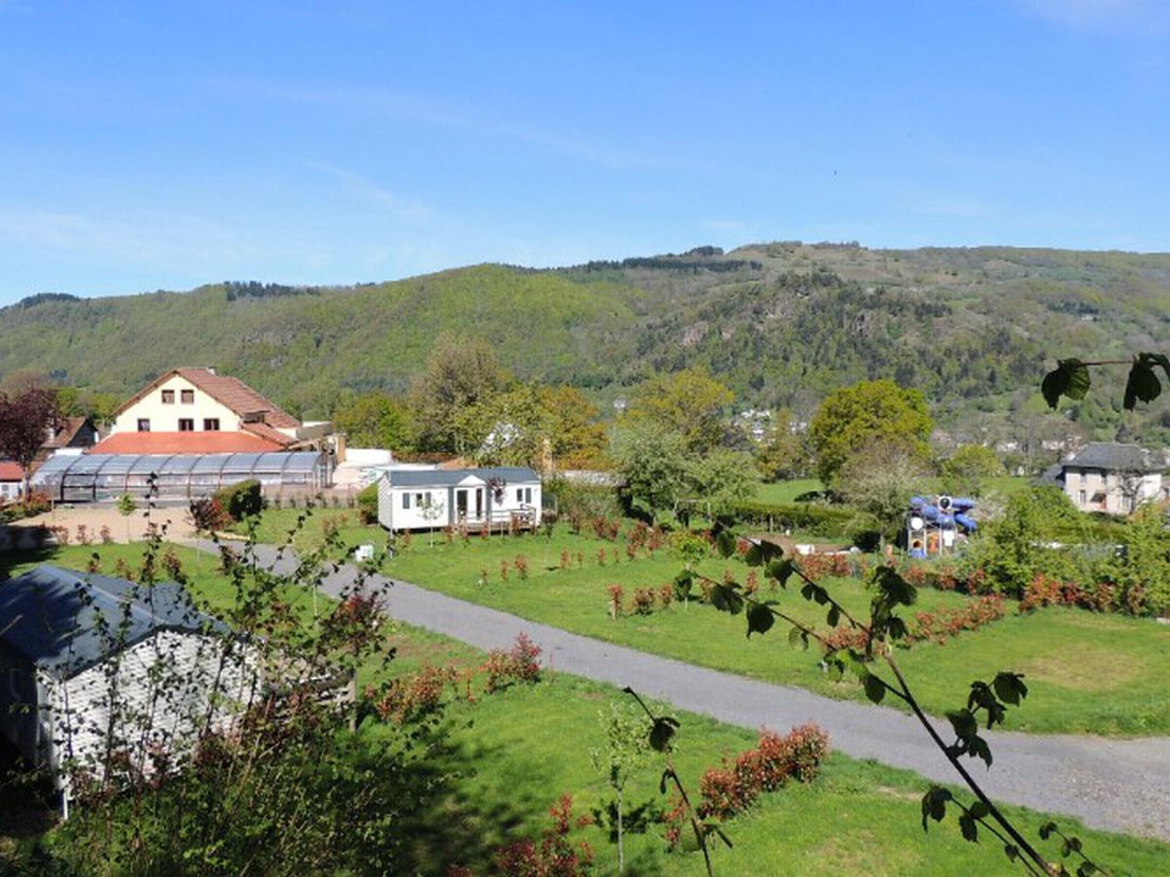 Un cadre rural avec une maison, une serre et un sentier qui traverse un paysage verdoyant.