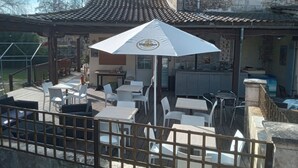 Une terrasse extérieure avec des chaises et des tables en plastique blanc, un grand parasol blanc et un bâtiment en pierre en arrière-plan.
