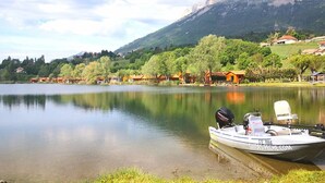 A calm lake with a boat docked on the shore, surrounded by houses and a mountain in the background.