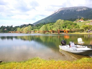 Un lac paisible, avec un bateau amarré sur la rive, entouré de maisons et avec une montagne en arrière-plan.