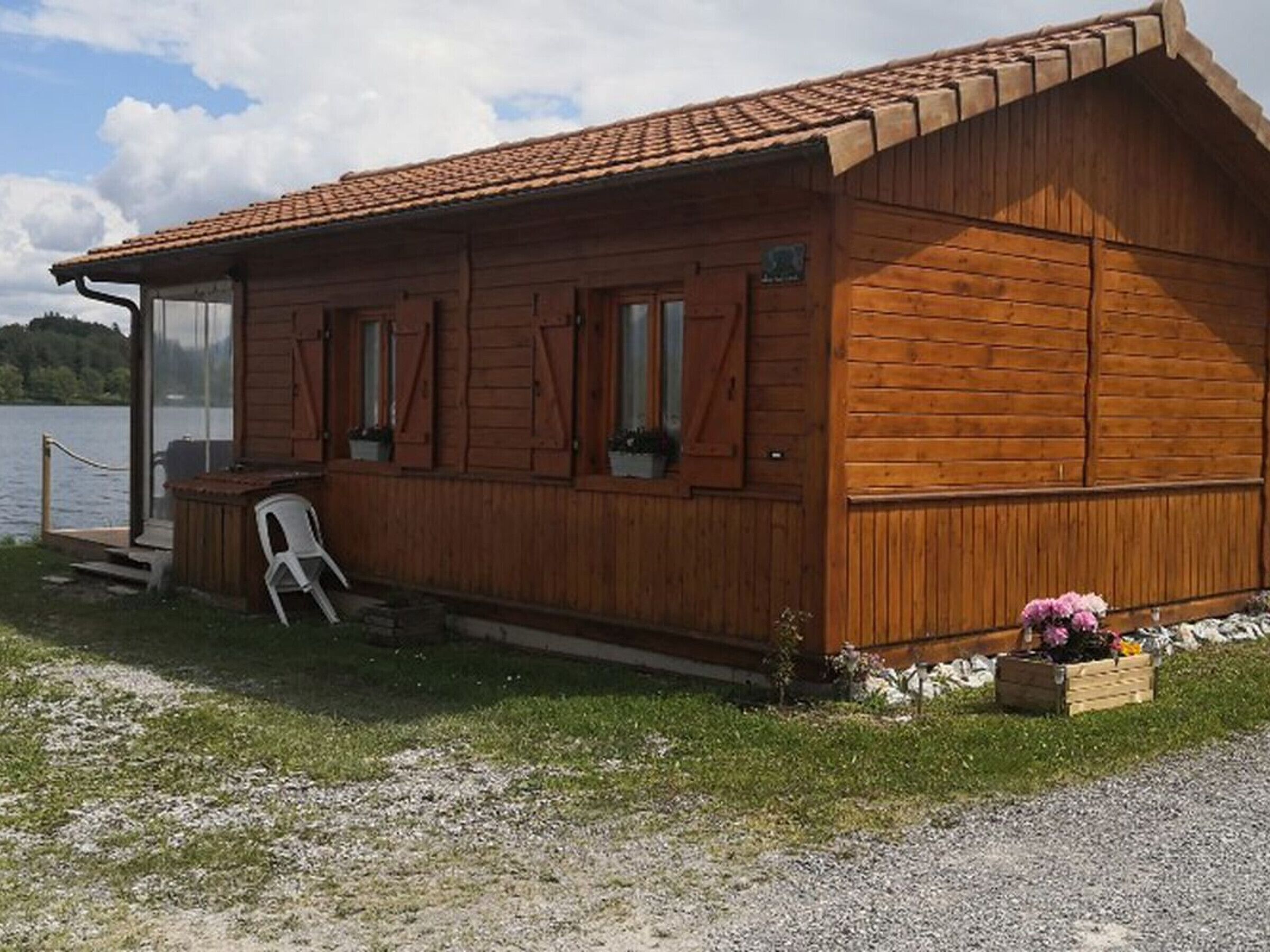 Eine Holzhütte mit geneigtem Dach, einer Veranda mit einem Stuhl und einem kleinen Garten mit Blumen.