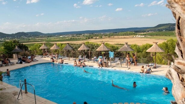 A pool with lounge chairs and umbrellas, surrounded by a stone wall and a view of the countryside. - Comfortable mobile home in Calvisson for 4 people (Calvisson)