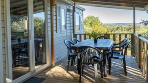 A covered outdoor patio with a table and chairs, a wooden deck, and a view of the surrounding landscape. - Comfortable mobile home in Calvisson for 4 people (Calvisson)
