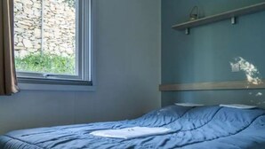 A bedroom with a bed, a window, and a stone wall outside. - Comfortable mobile home in Calvisson for 4 people (Calvisson)