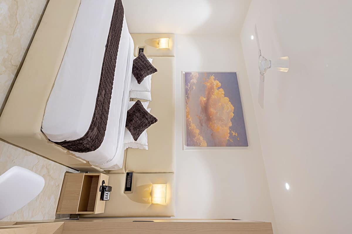 Una habitación de hotel moderna con cama, mesita de noche, espejo, obra de arte y un pequeño baño.