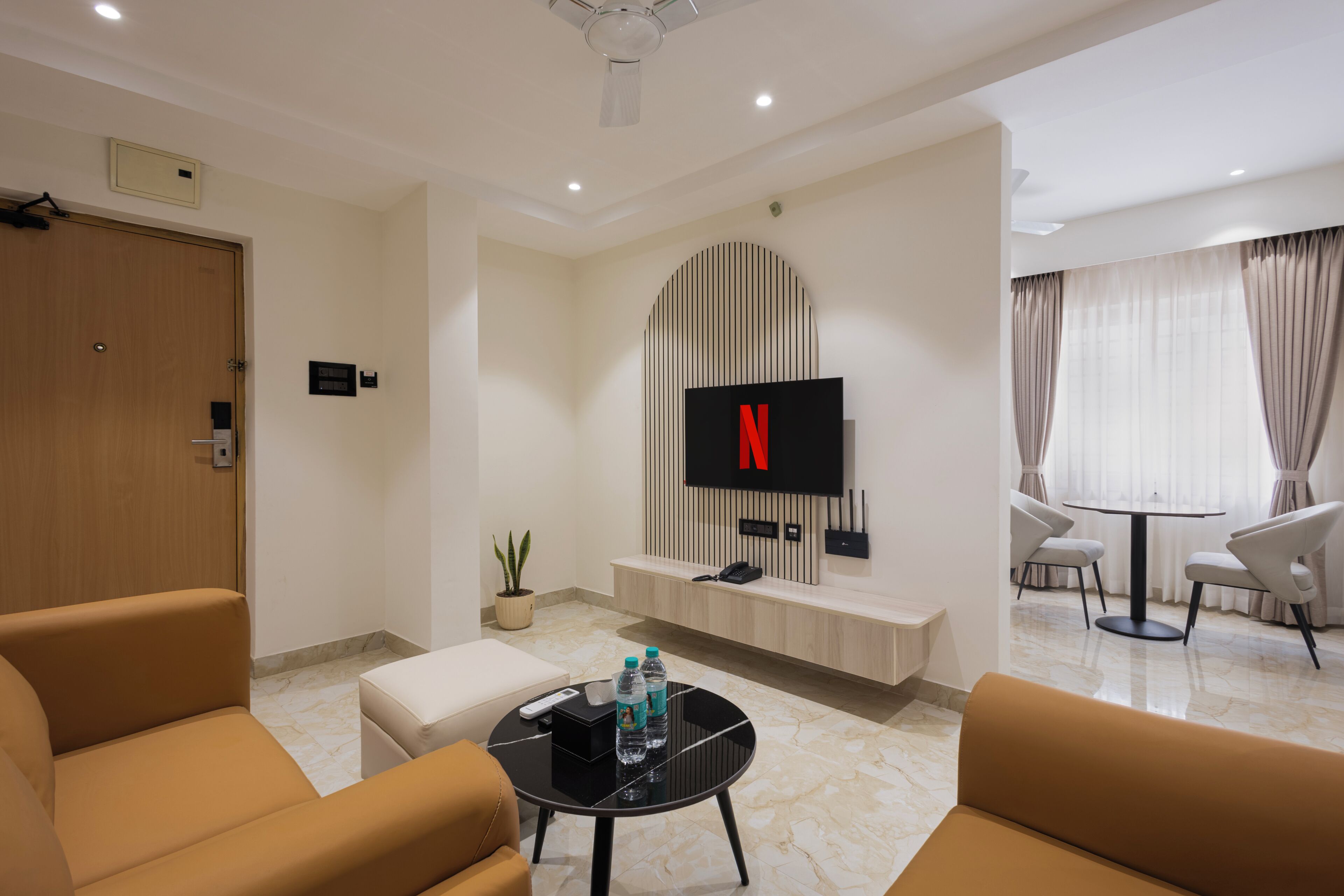 A modern living room with a flat-screen TV mounted on the wall, a coffee table with water bottles, and a seating area with sofas.